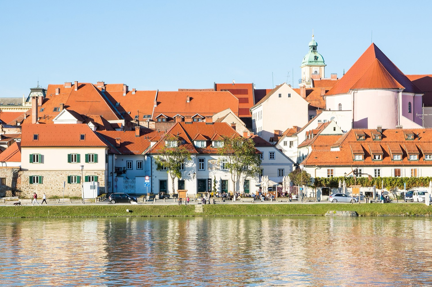 The Drava riverfront promenade at Lent — the old riverside houses, cafe terraces and the Judgement Tower in summer sun